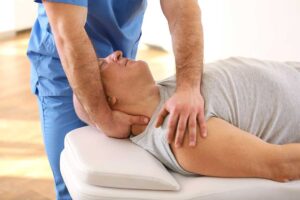 A chiropractor gently adjusts a patient's back in a bright, clean treatment room.